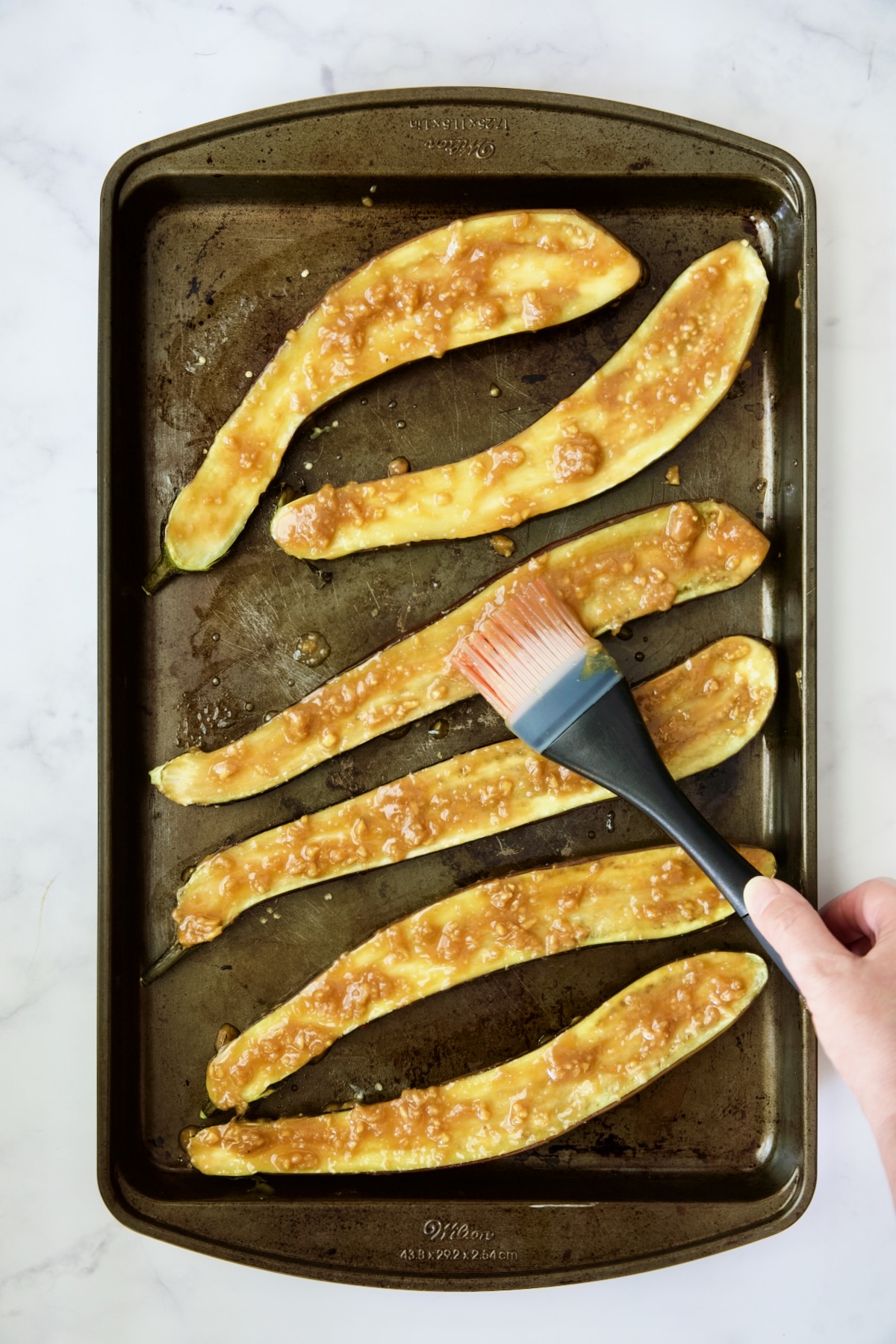 Six Japanese eggplant halves being brushed with glaze.