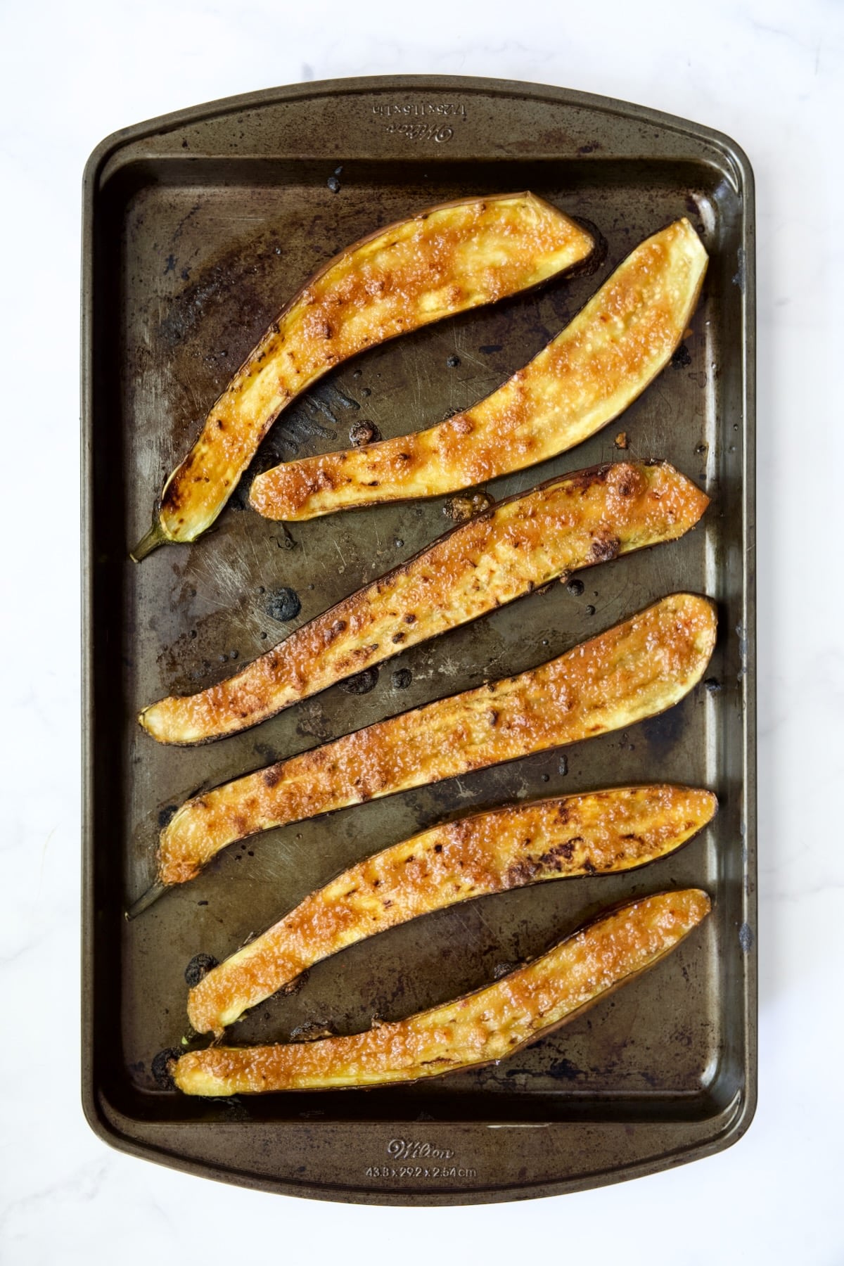 Six broiled Japanese eggplant halves on stainless steel rimmed baking sheet.