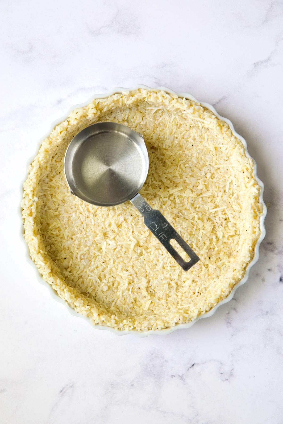 Unbaked brown rice crust with 1-cup measuring cup pressing crust.