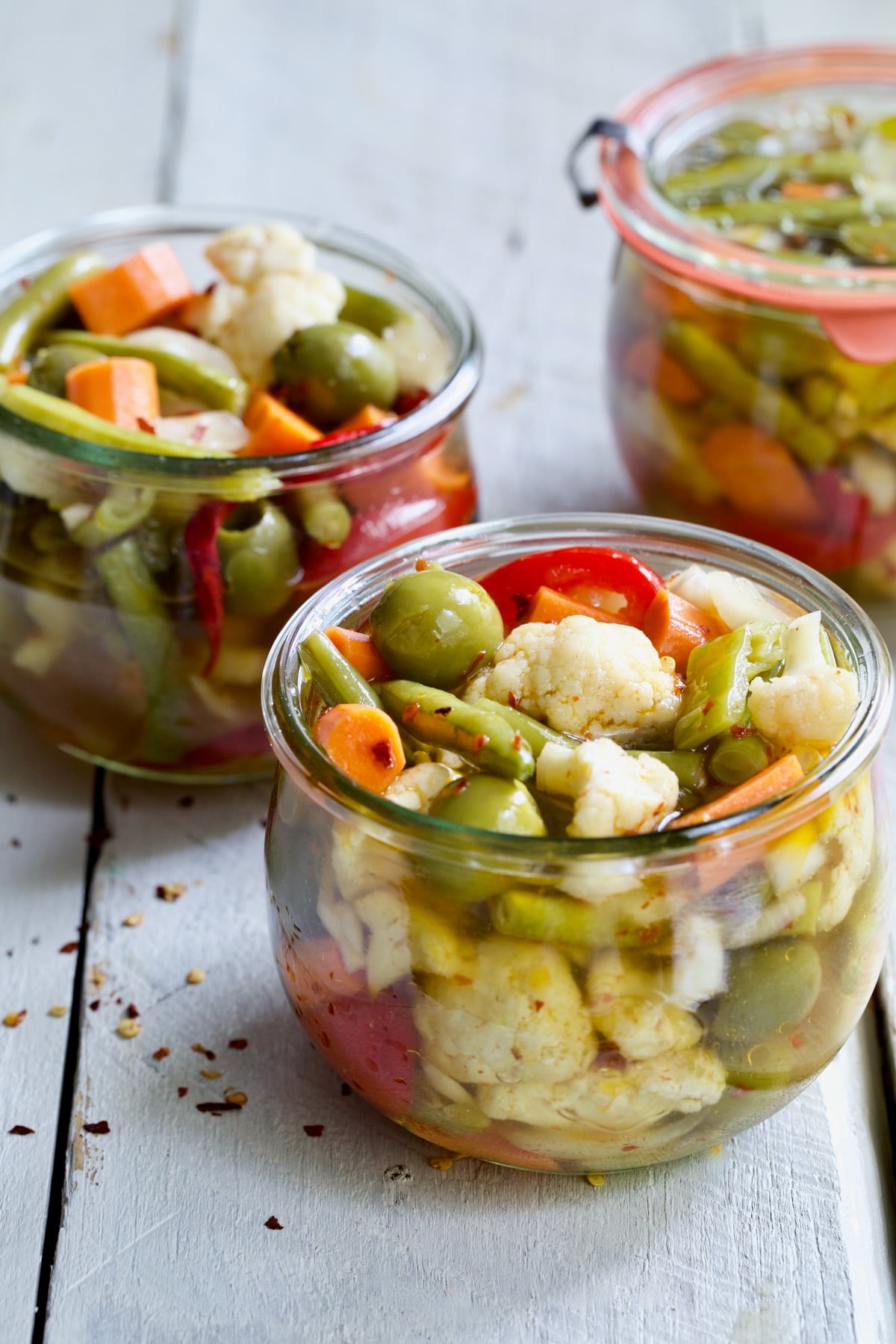 Three jars of Giardiniera (Italian Pickled Vegetables) on white wood surface.