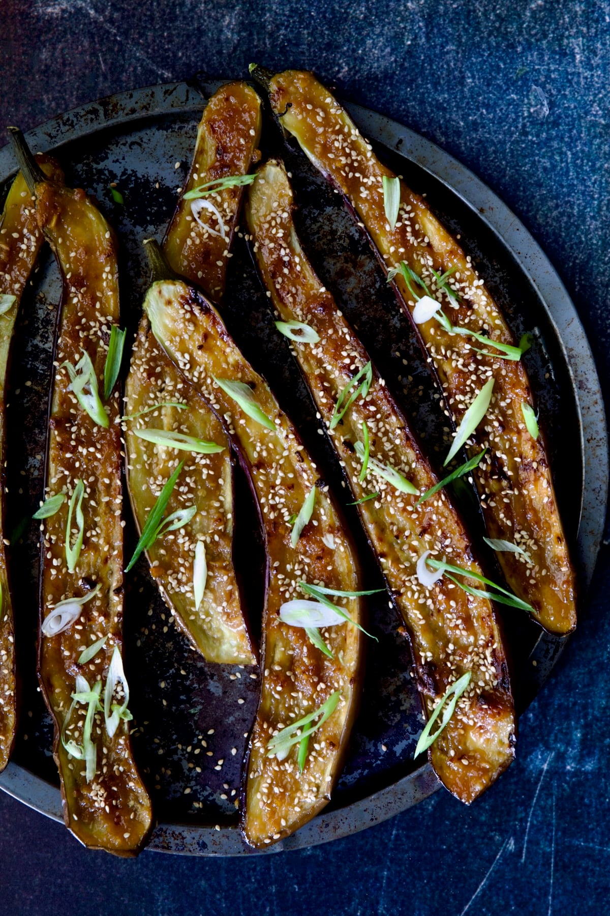 Miso-Glazed Eggplant on round metal pan garnished with scallions and sesame seeds.