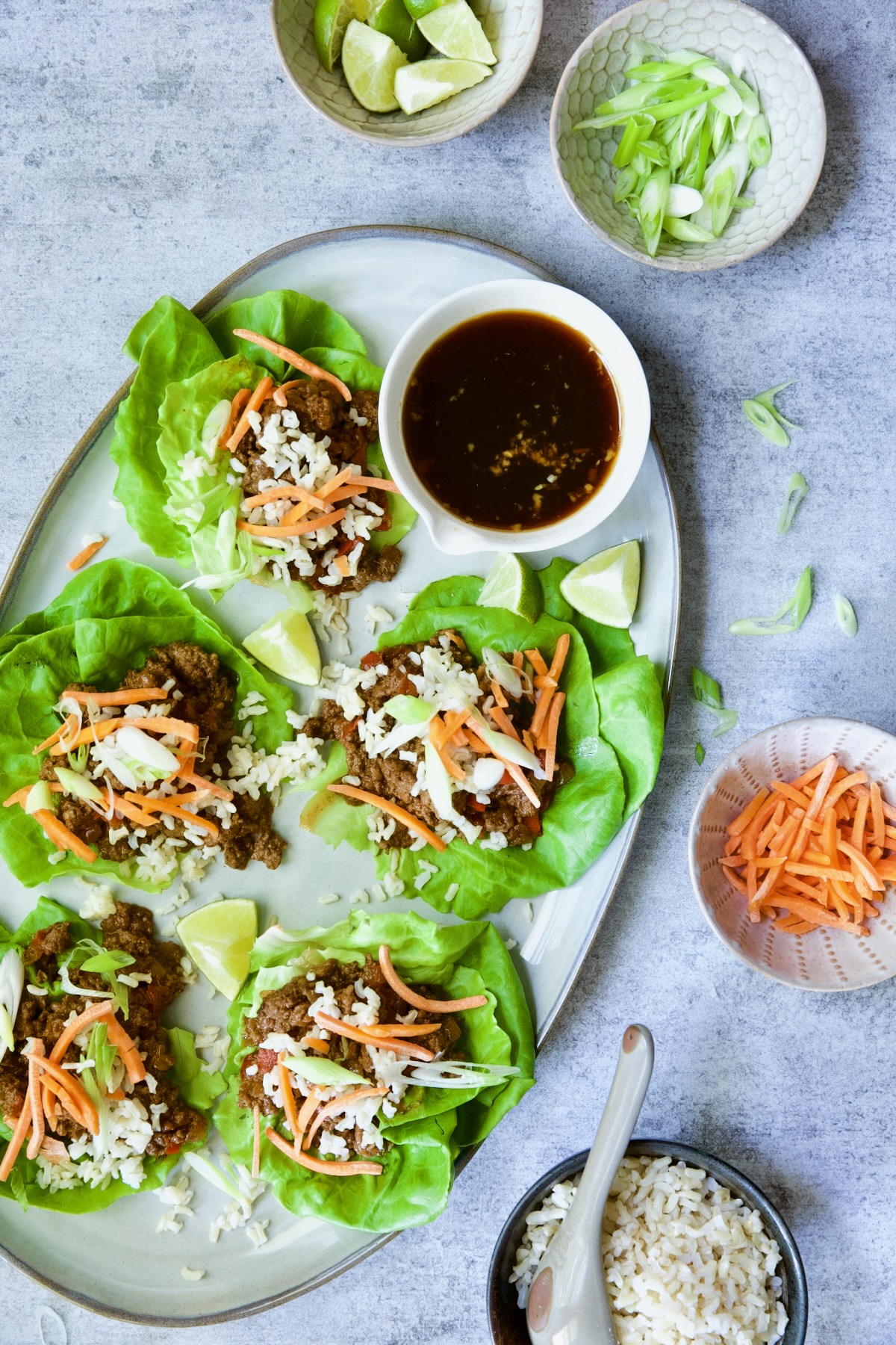 Beef Lettuce Wraps Recipe with Lime Ginger Dipping Sauce with toppings of lime wedges, scallion, carrot and brown rice.