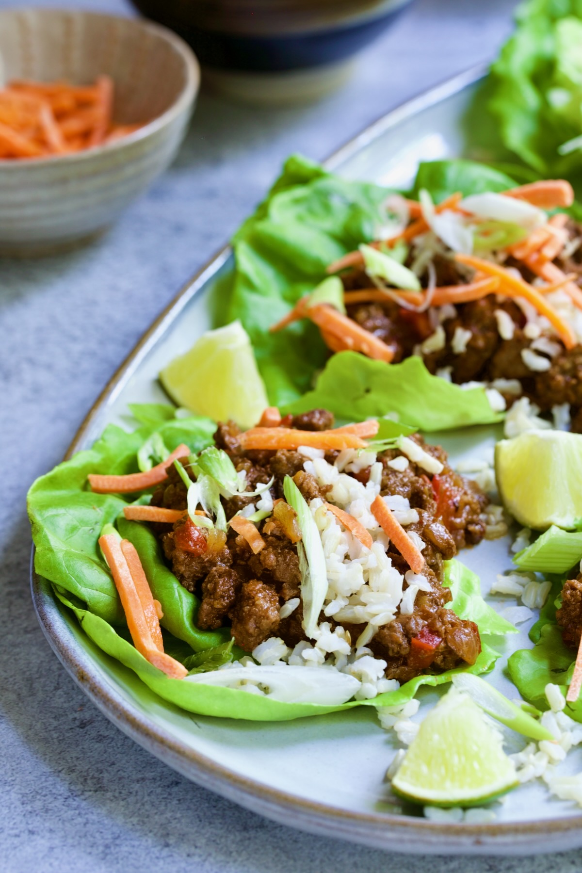 Beef Lettuce Wraps on gray platter garnished with shredded carrots and scallions.