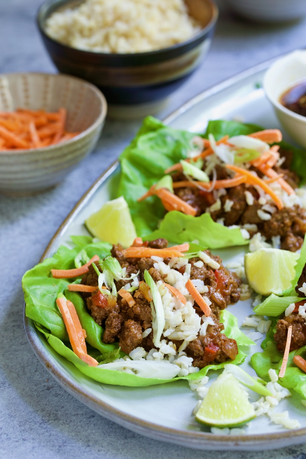 Beef Lettuce Wraps Recipe with Lime Ginger Dipping Sauce with lime wedges on gray platter.