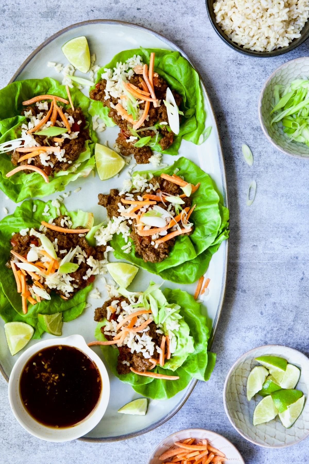 Assembled Beef Lettuce Wraps Recipe with Lime Ginger Dipping Sauce with lime wedges on gray platter.