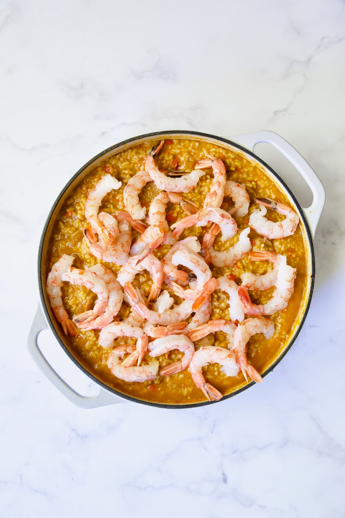 Process shot of paella with shrimp added.