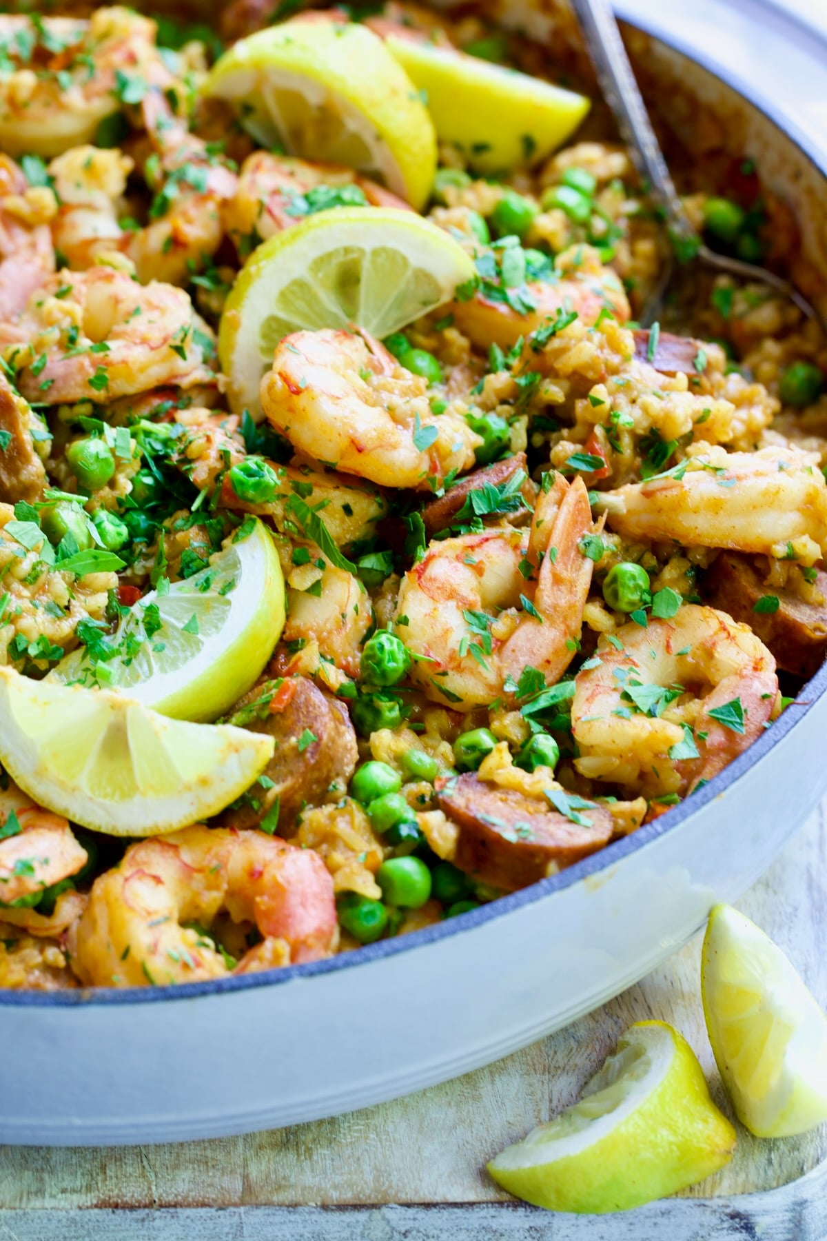 Brown Rice Paella with Shrimp and Chorizo with lemon wedges in white cast iron enamel skillet.