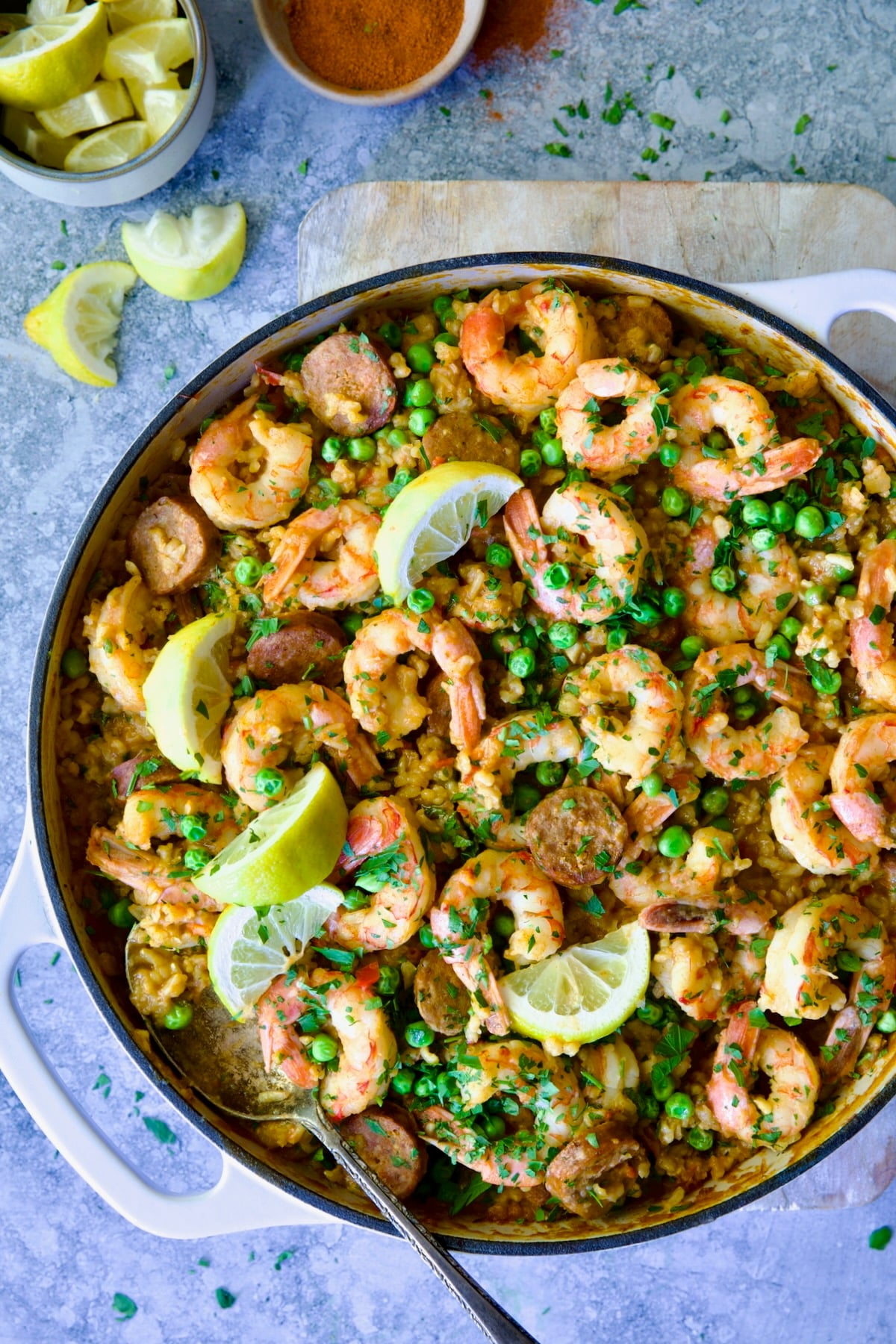 Brown Rice Paella with Shrimp and Chorizo in white enamel cast iron skillet on wood cutting board.