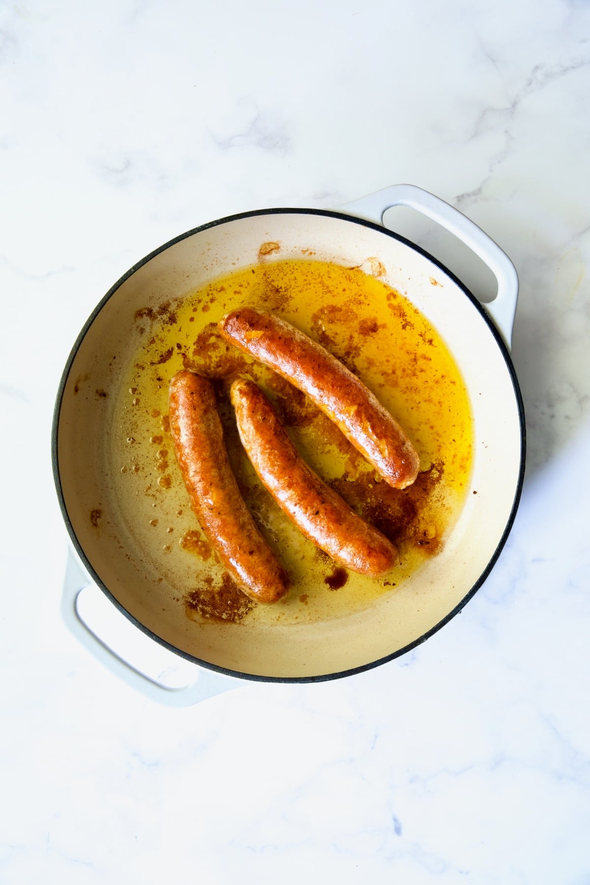 Three cooked chorizo links in white enamel cast iron skillet.