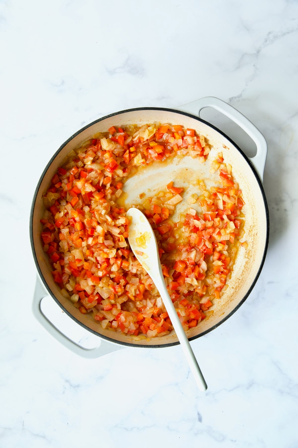 Process shot of cooked onions, bell pepper and tomatoes.