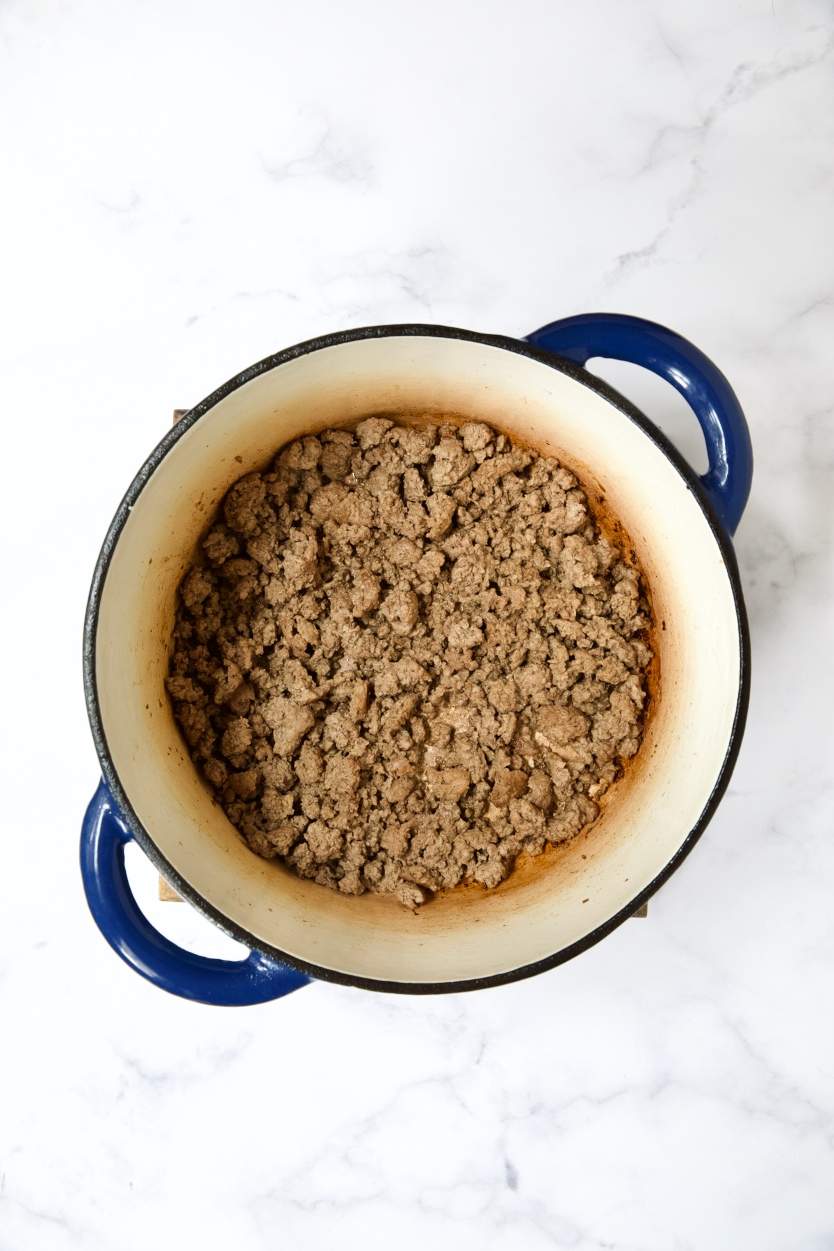 Cooked ground beef in blue Dutch oven.
