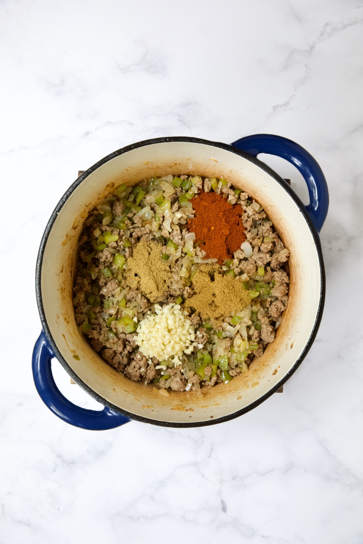 Spices added to ground beef, peppers and onions in blue Dutch oven.