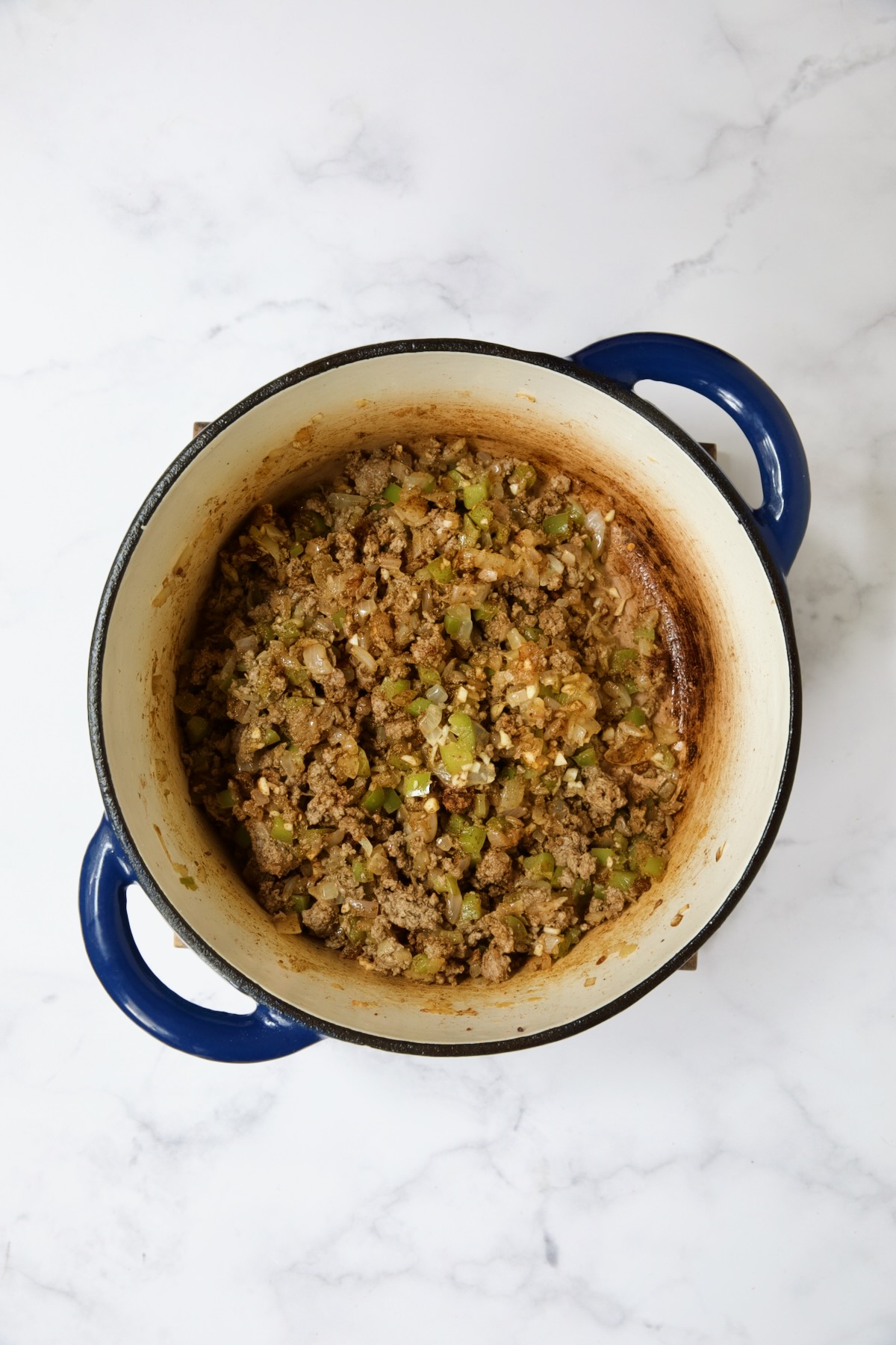 Ground beef, peppers and onions in blue Dutch oven.