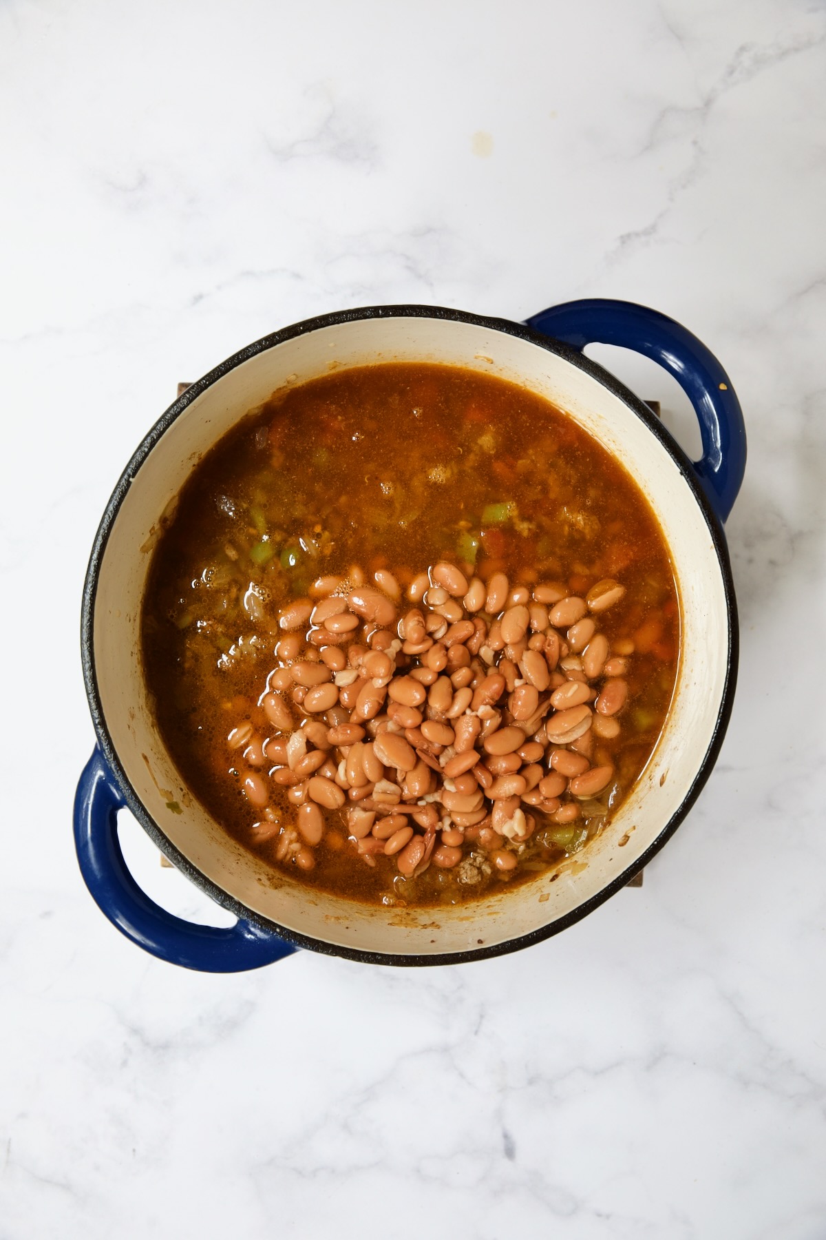 Beans added to soup in blue Dutch oven.