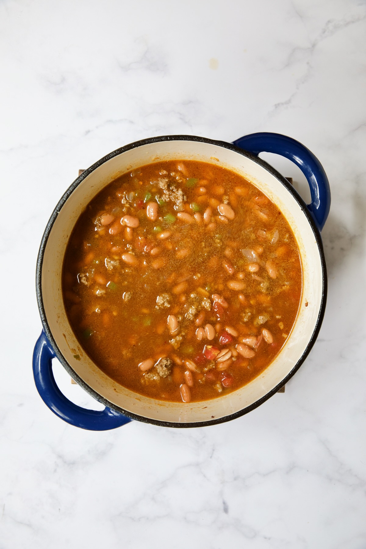 Soup with beans and beef in blue Dutch oven.