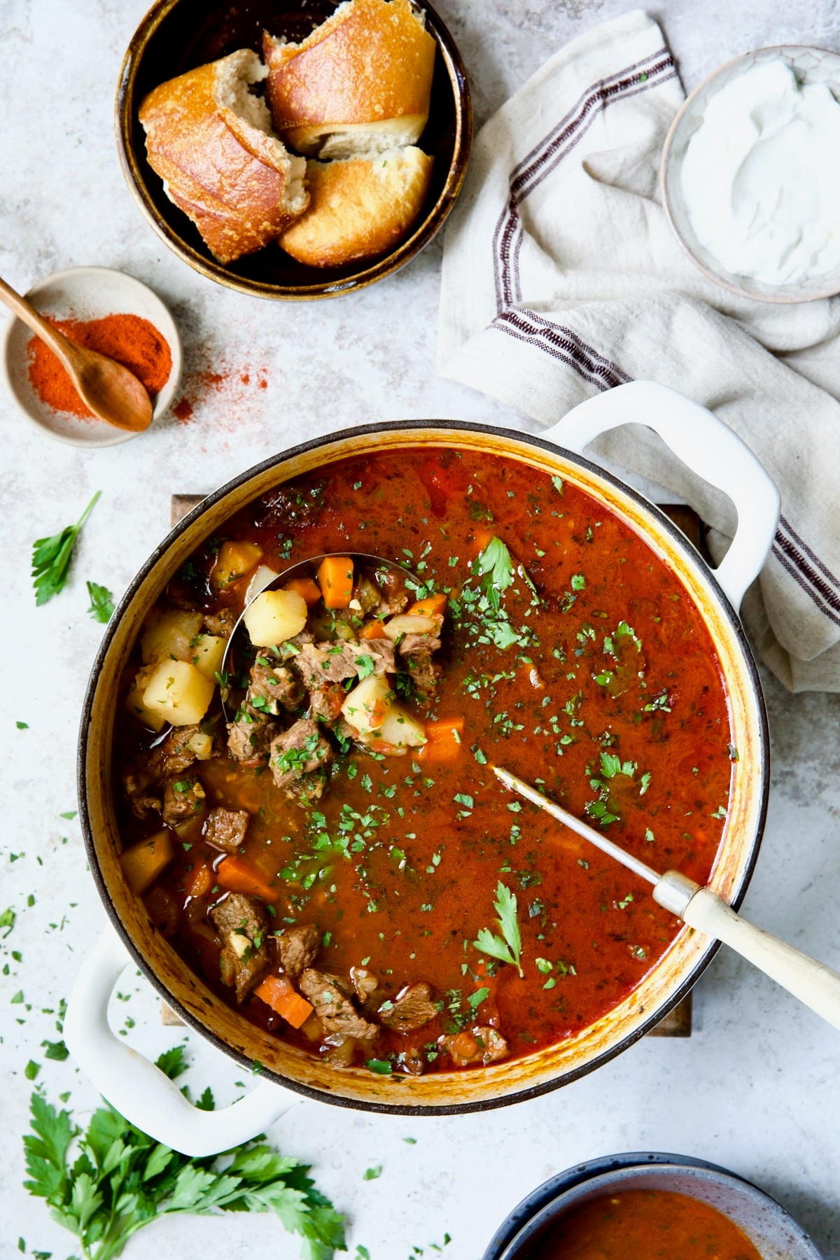 Traditional Hungarian Goulash Recipe in white Dutch oven garnished with fresh parsley.