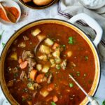 Finished Traditional Hungarian Goulash Soup Recipe in white Dutch oven with bread and sour cream.