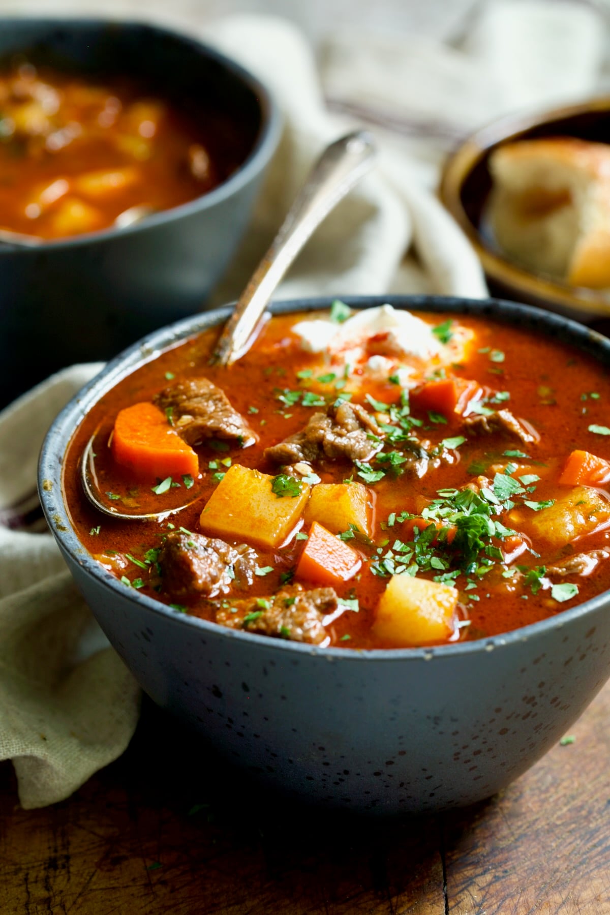 Traditional Hungarian Goulash Soup Recipe in gray bowl with a piece of carrot and beef soup spoon.