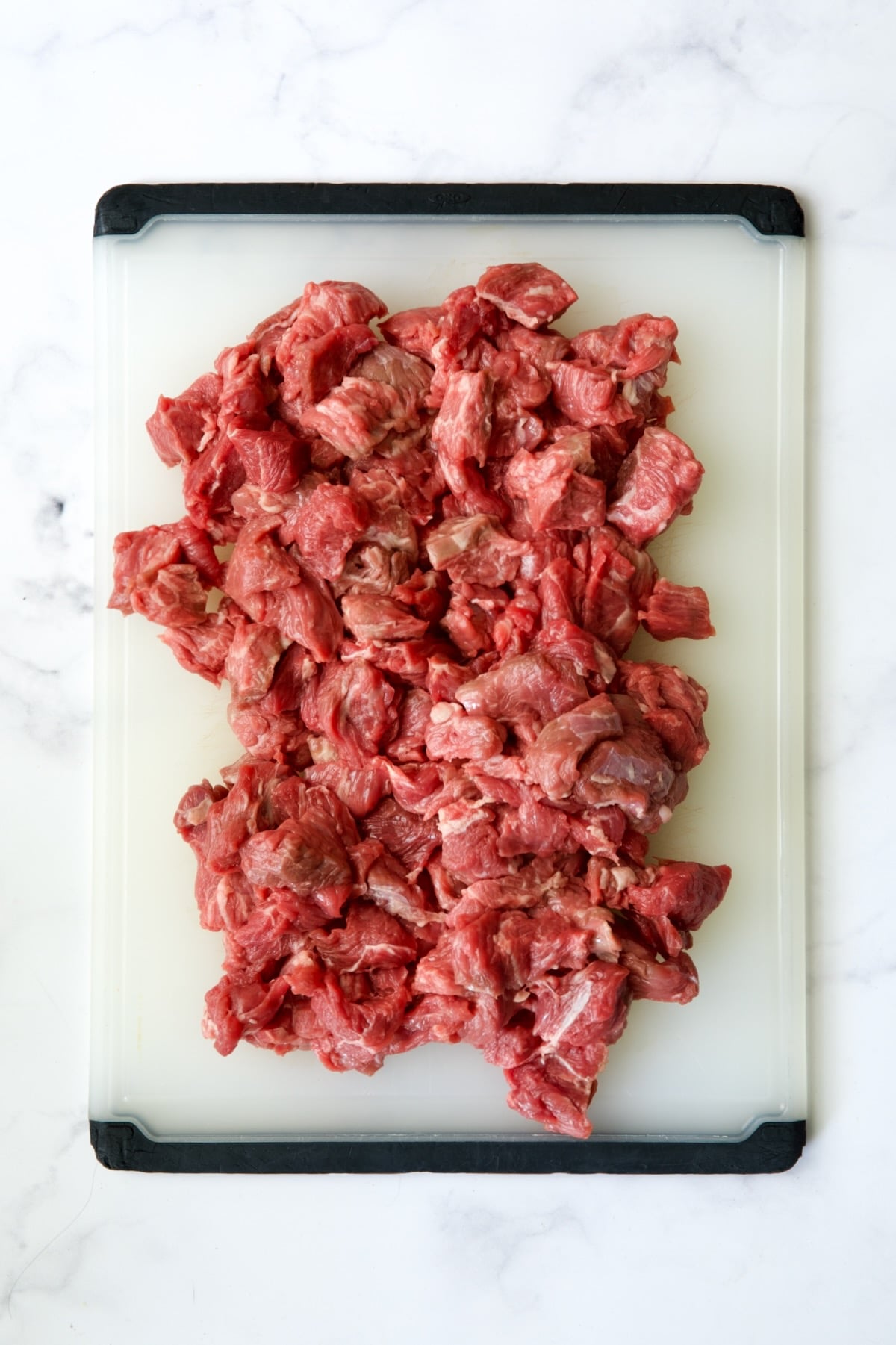 Pieces of beef on white plastic cutting board.