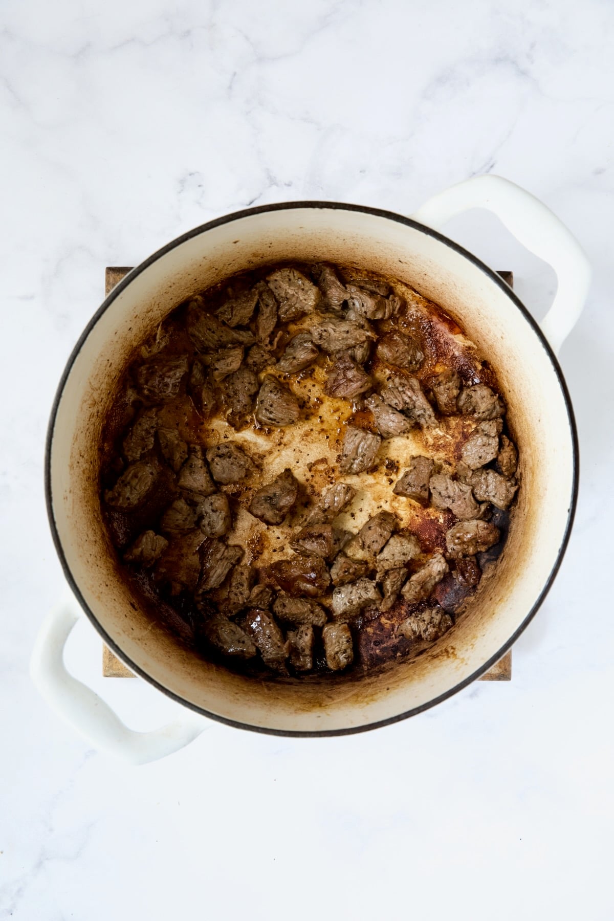 Browned pieces of beef in white Dutch oven.