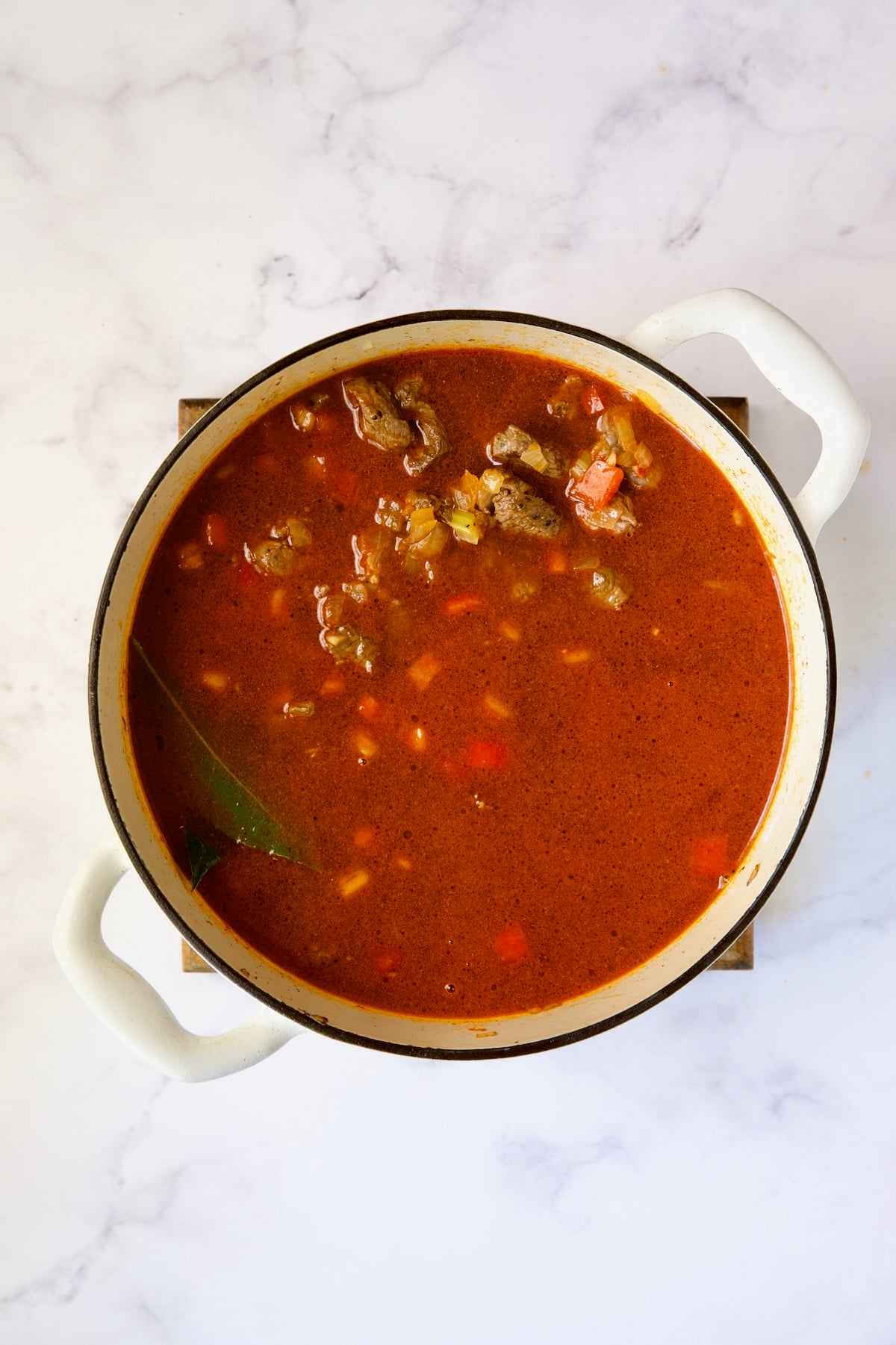 Beef added to goulash in white Dutch oven.