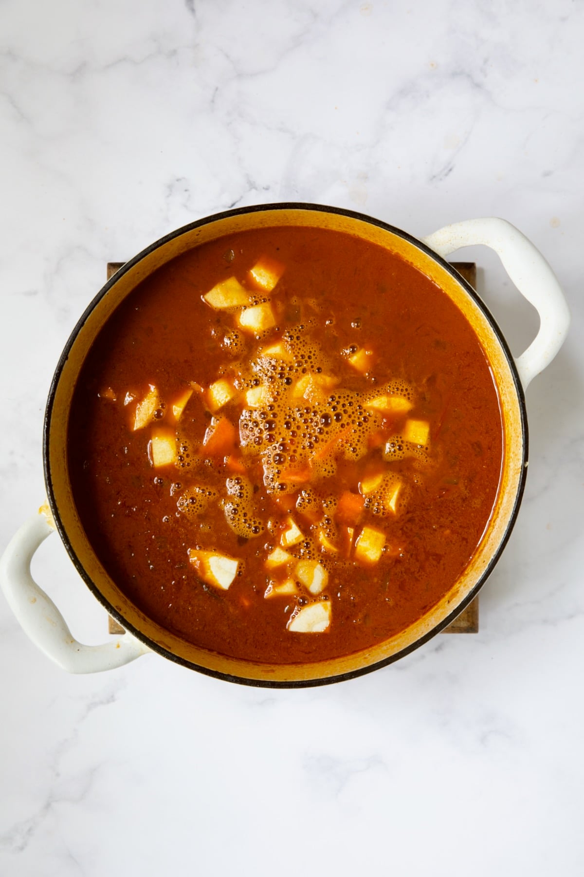 Carrots and parsnips added to goulash in white Dutch oven.