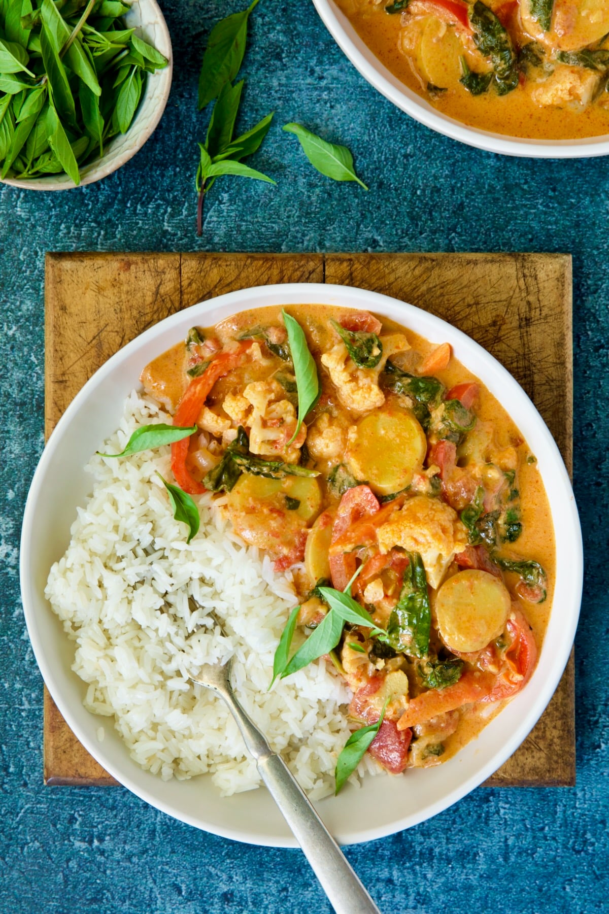 Bowl of vegetable curry with rice garnished with fresh basil.