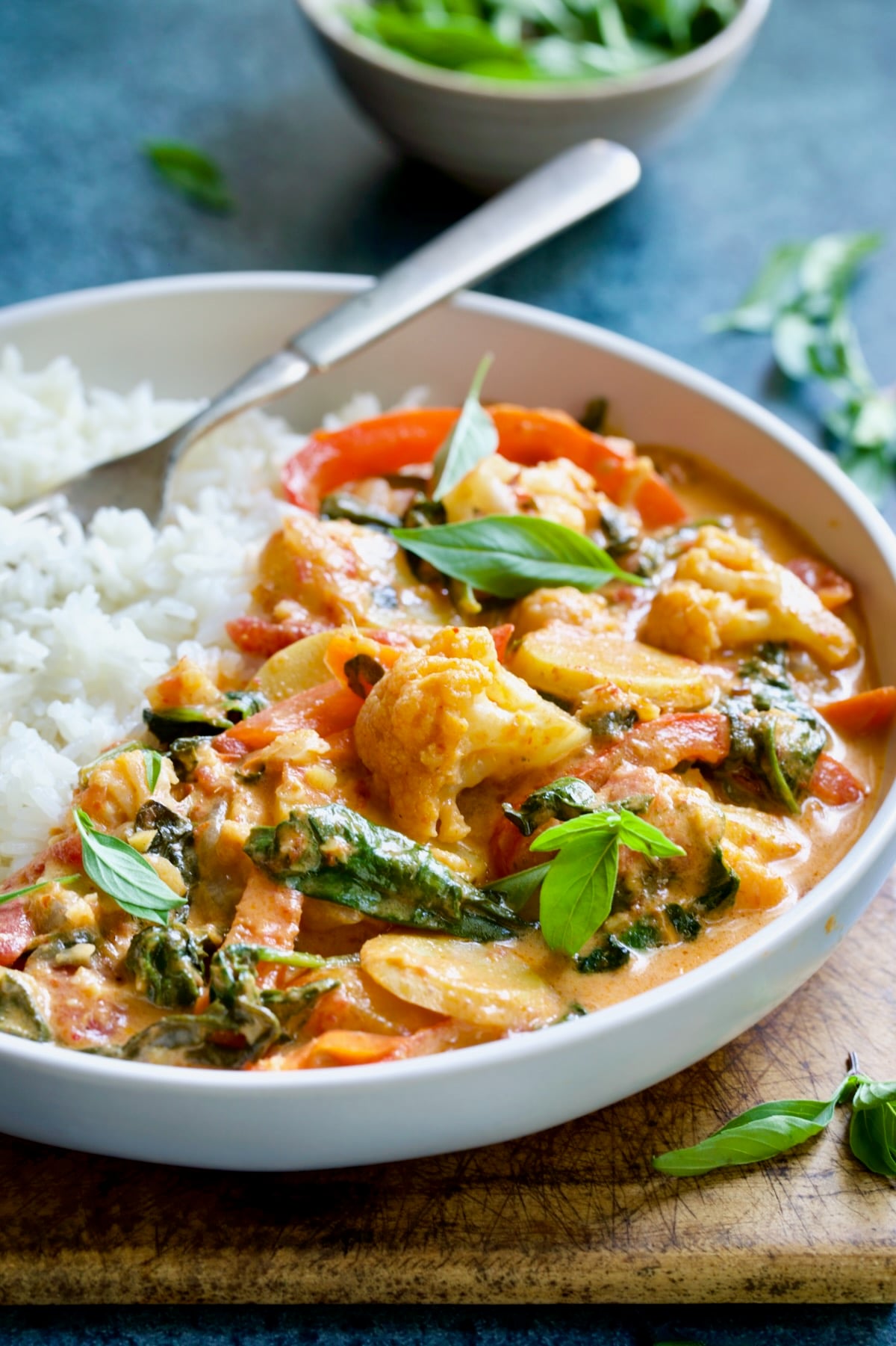 Vegetable curry in white bowl with rice garnished with fresh basil.