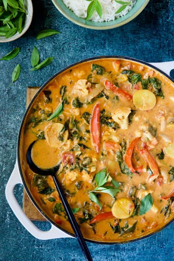 Vegan Thai Red Curry in white enamel cast iron skillet with black serving spoon.