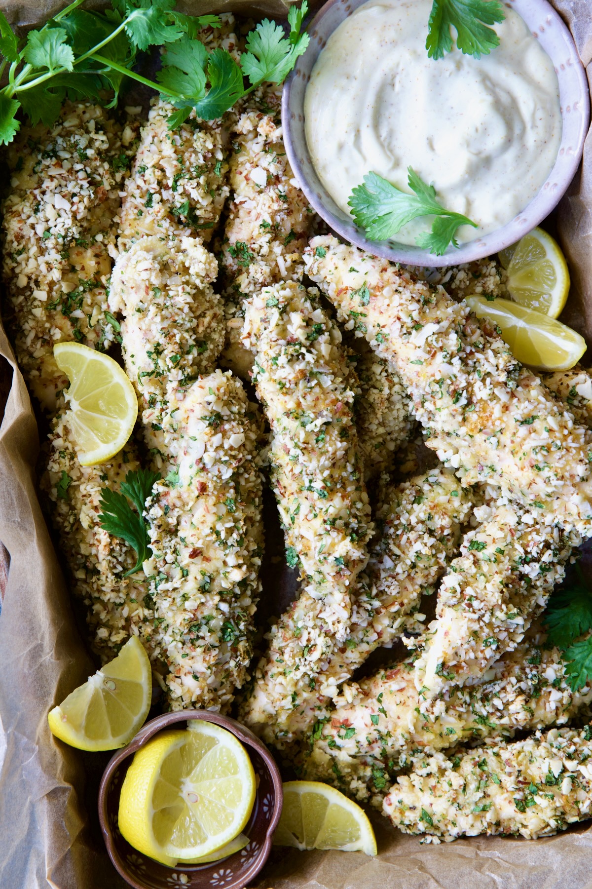Almond-Crusted Chicken Tenders with Lemon Curry Mayonnaise with cilantro sprigs and lemon wedges.