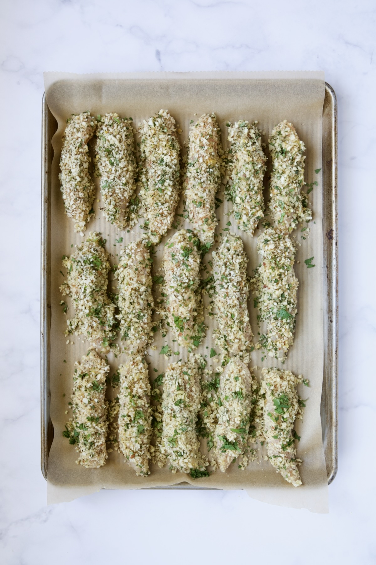 Almond coated chicken tenders on parchment paper-lined rimmed baking sheet.