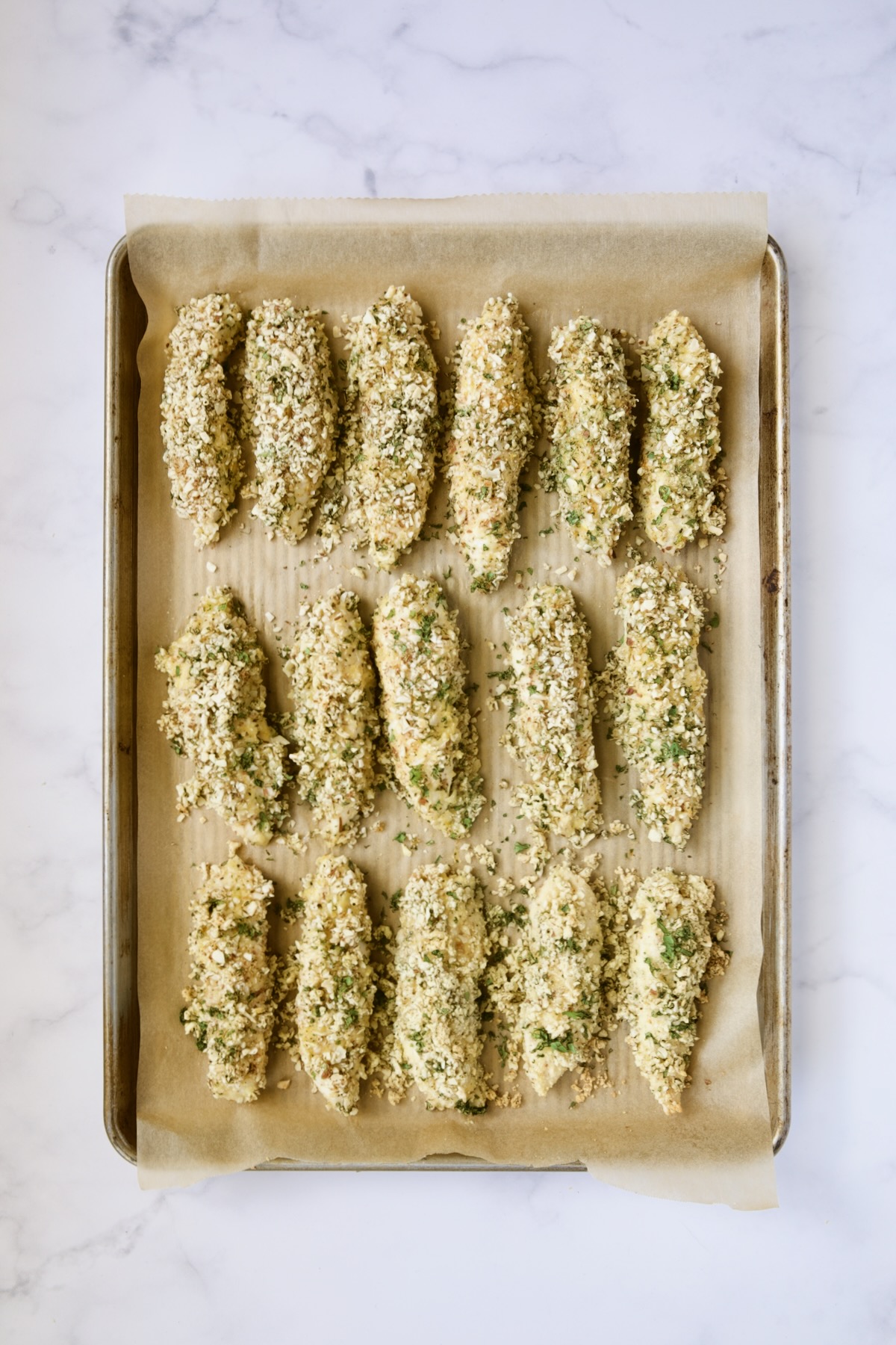 Baked almond coated chicken tenders on parchment paper-lined rimmed baking sheet.