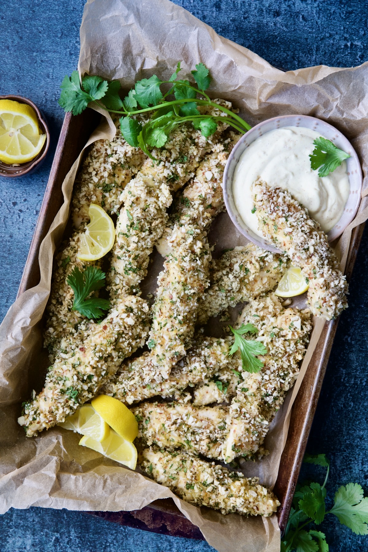 Almond-Crusted Chicken Tenders with Lemon Curry Mayonnaise with one tender dipped into mayonnaise garnished with lemon and cilantro.