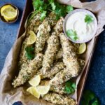Almond Chicken Tenders with Lemon Curry Mayonnaise in parchment paper-lined pan garnished with lemon wedges and cilantro.