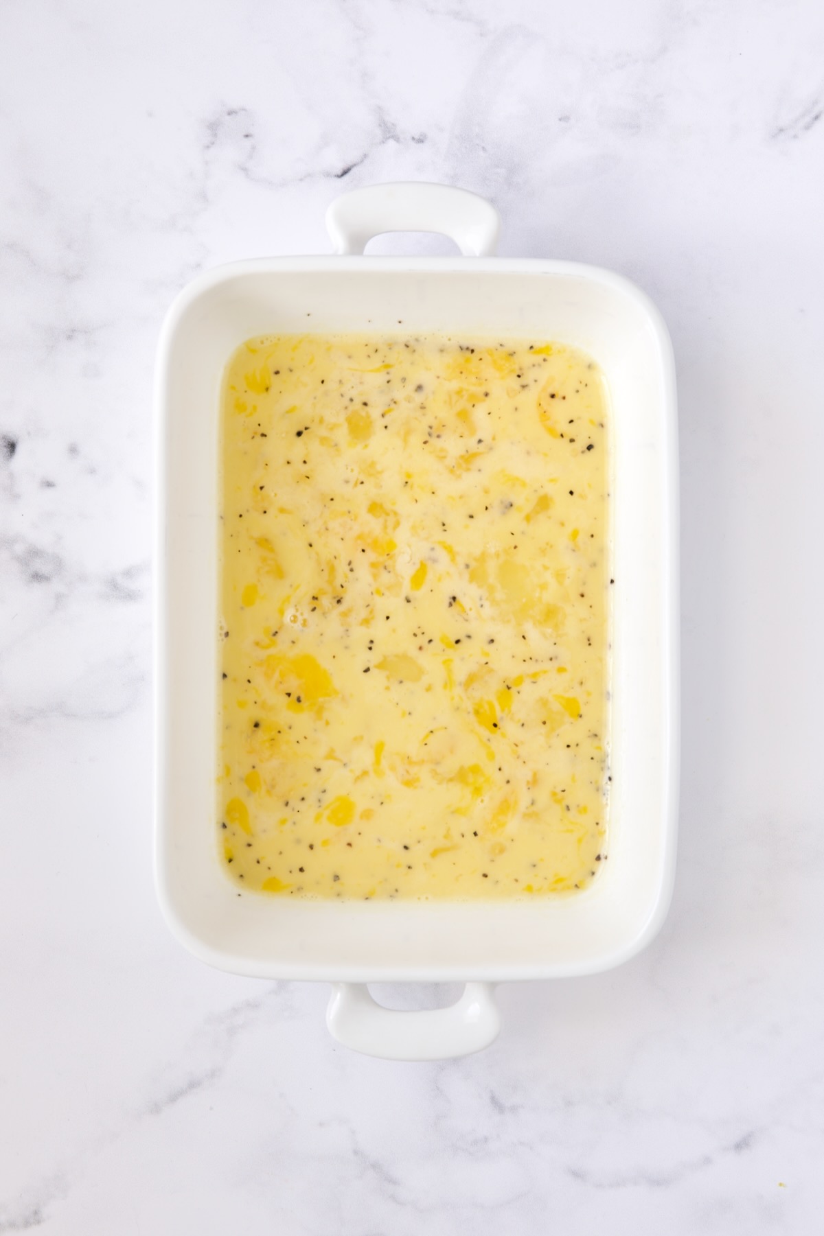 Seasoned beaten eggs in white rectangular pan.
