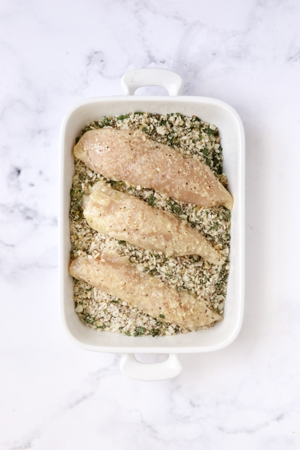 Three chicken tenders in almond coating in white rectangular baking pan.