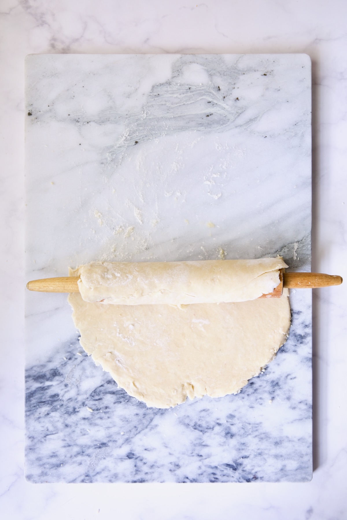 Galette dough being rolled onto rolling pin from marble pastry board.
