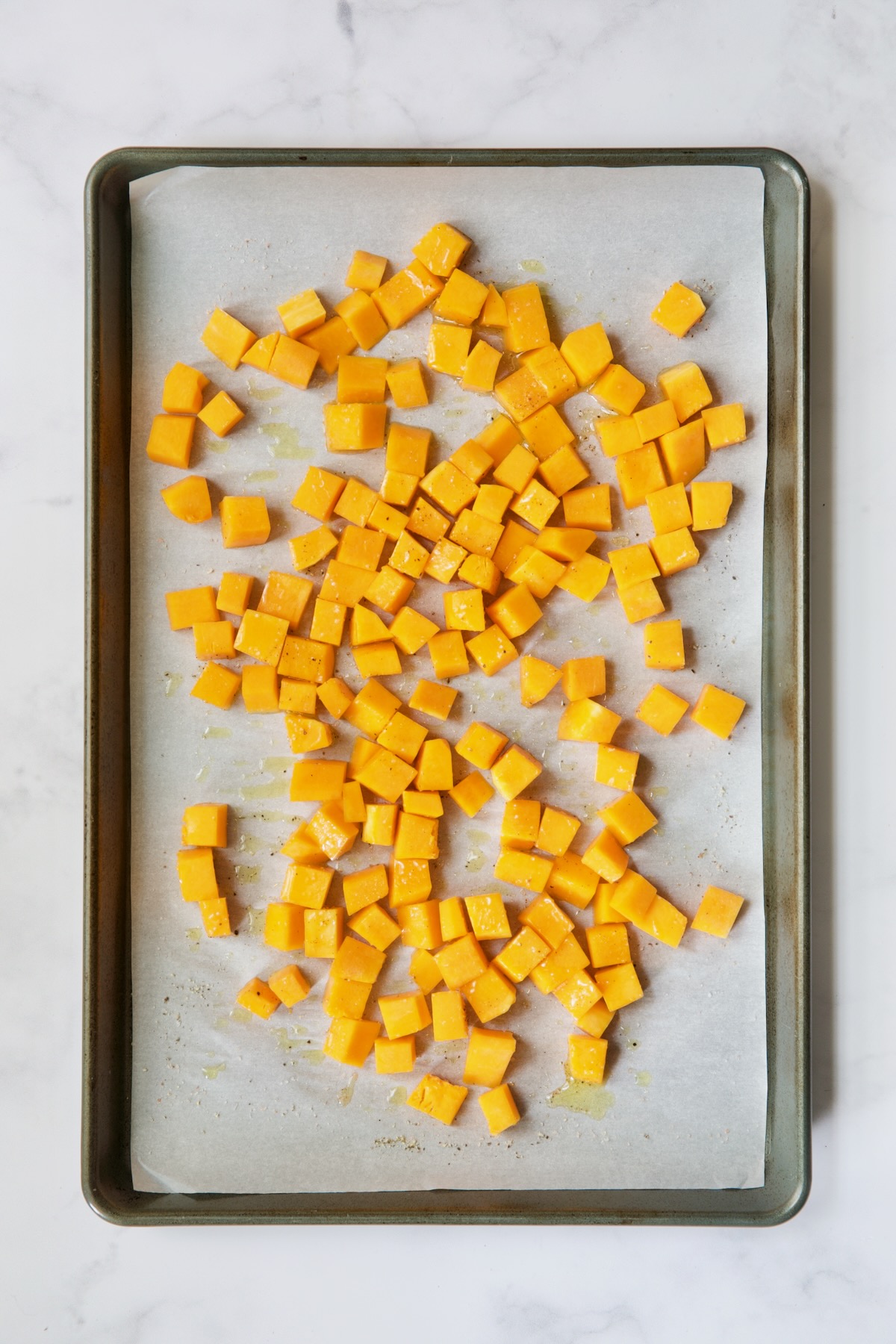 Butternut squash cubes on white parchment paper-lined baking sheet before being roasted.