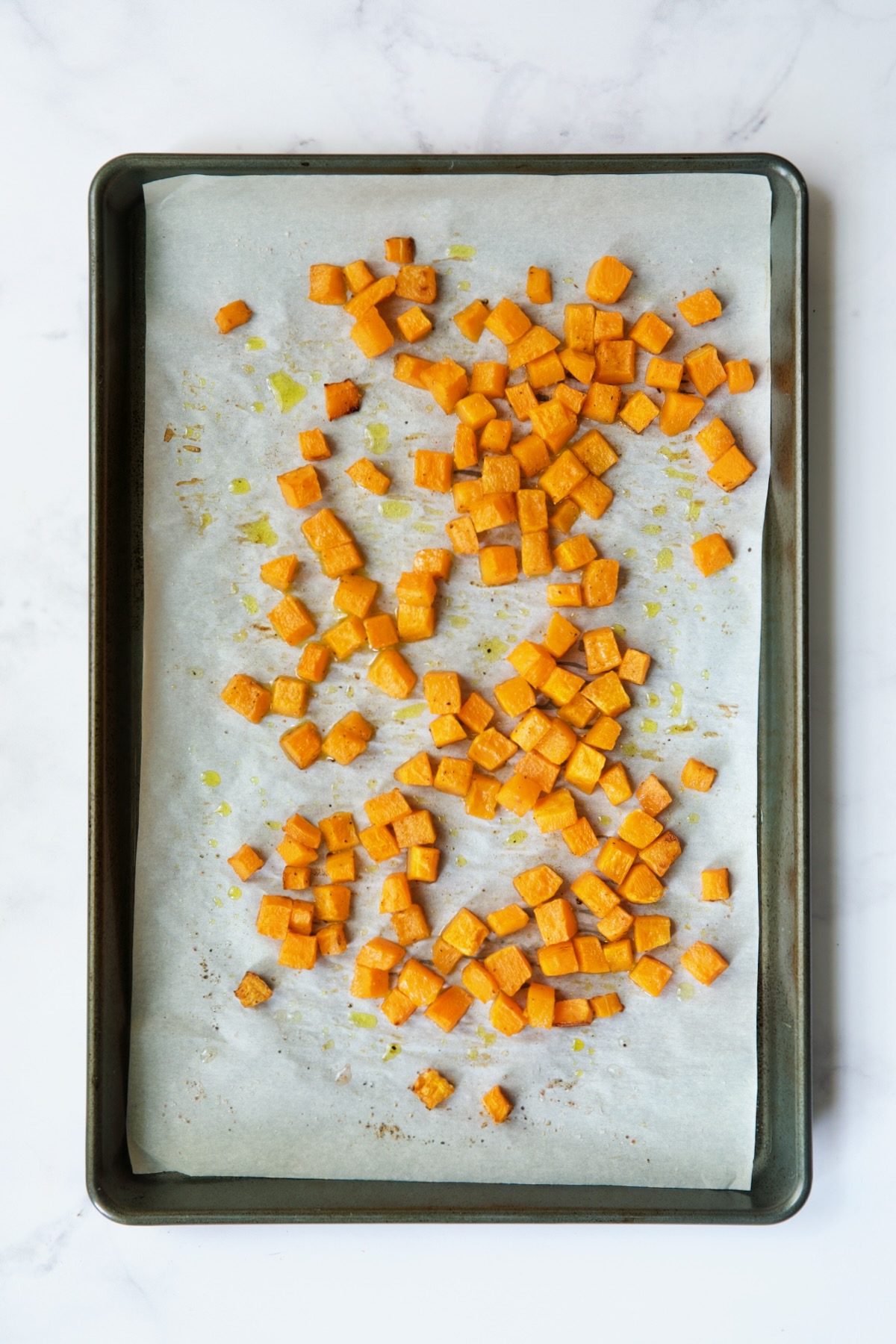 Roasted butternut squash cubes on white parchment paper lined baking sheet.