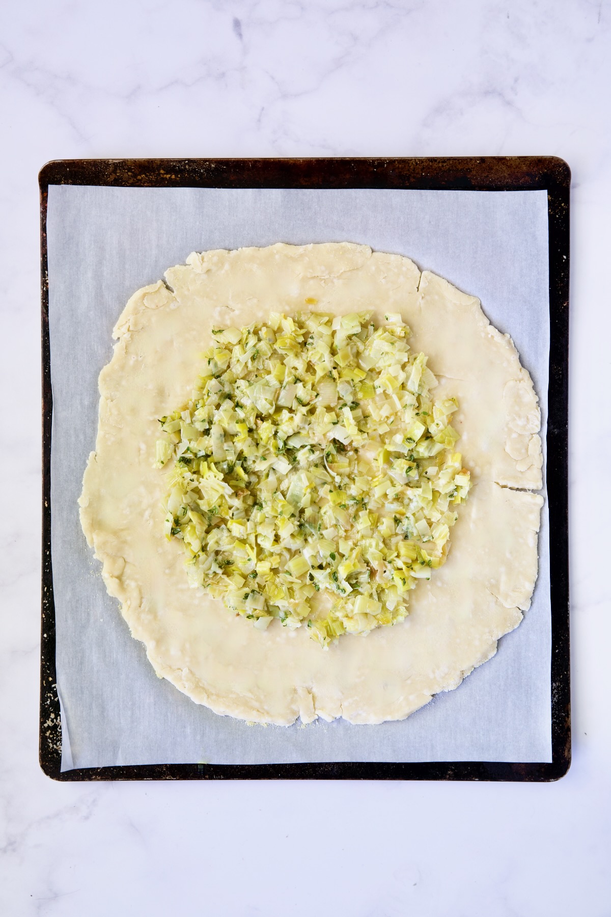 Leeks on galette dough on white parchment paper-lined baking sheet.