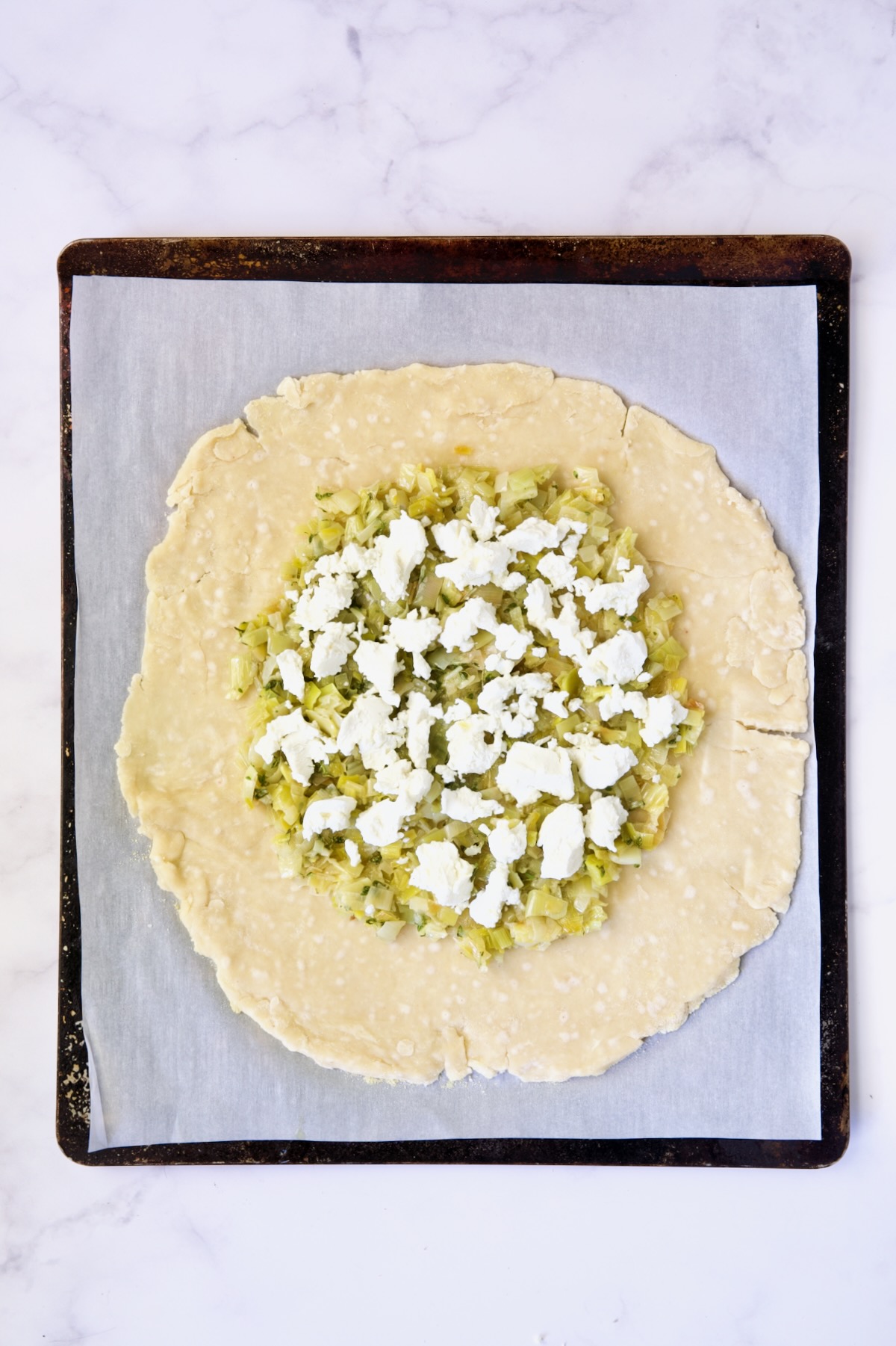Leeks and goat cheese on galette dough on white parchment paper-lined baking sheet.