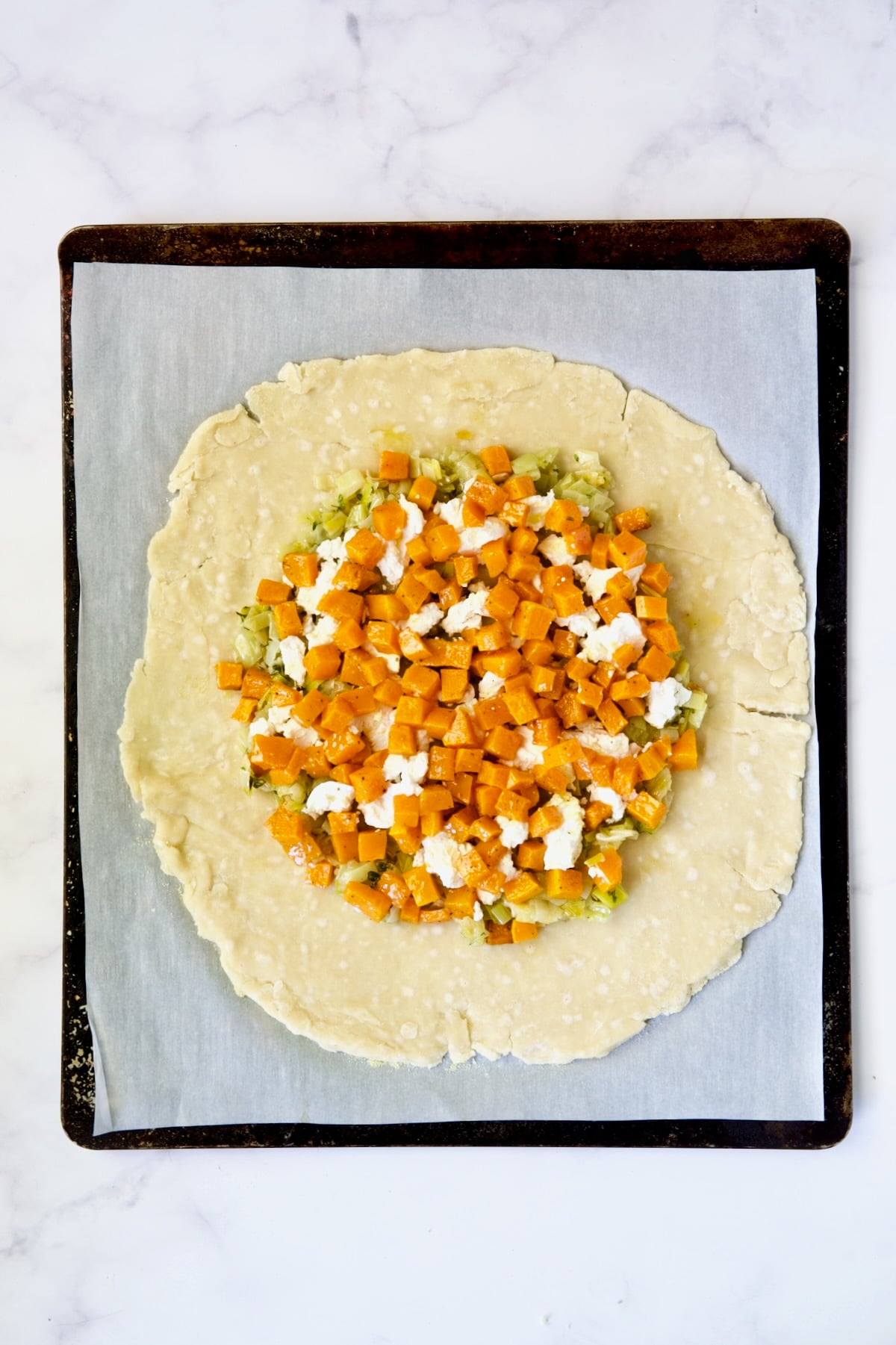 Butternut squash, goat cheese and leeks on galette dough on parchment paper-lined baking sheet.