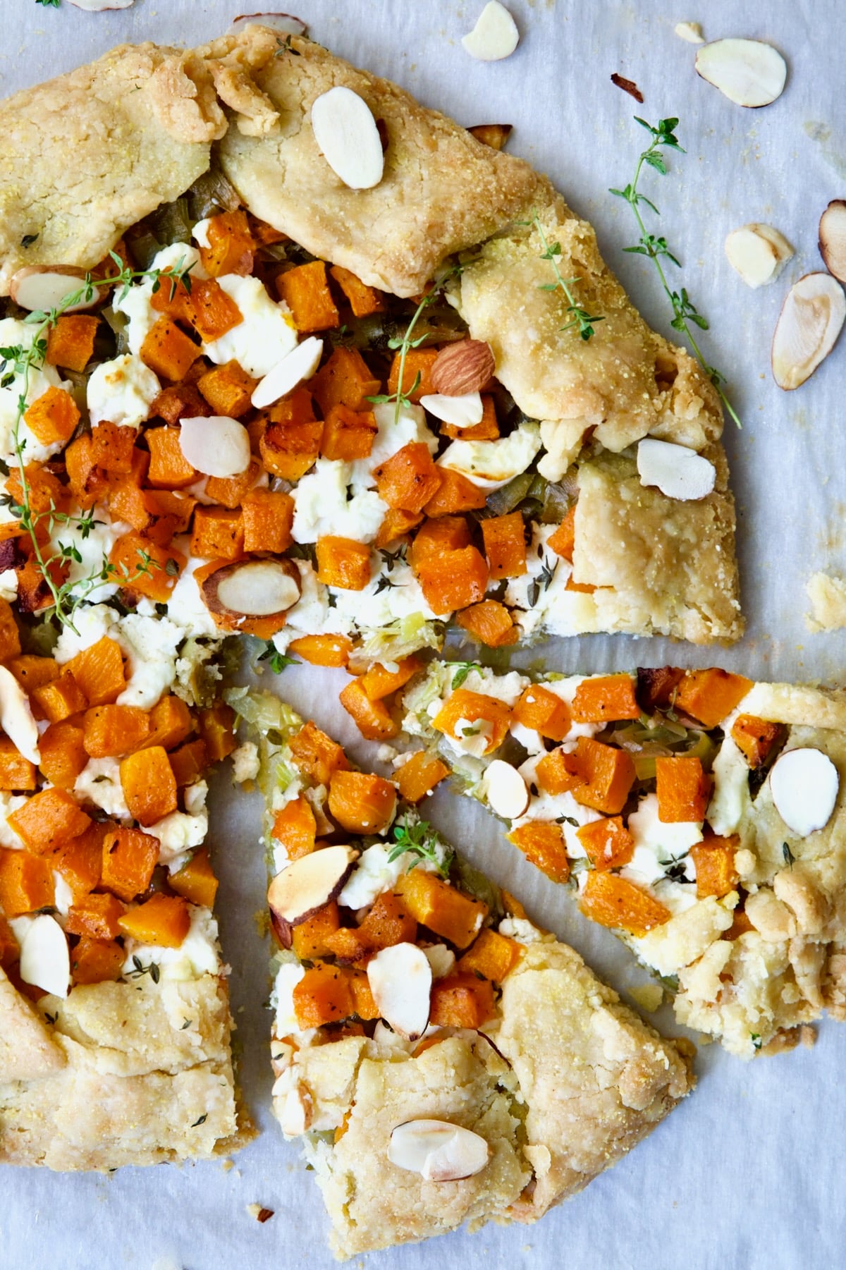 Butternut Squash Leek and Goat Cheese Galette on white parchment paper garnished with sliced almonds and fresh thyme sprigs.