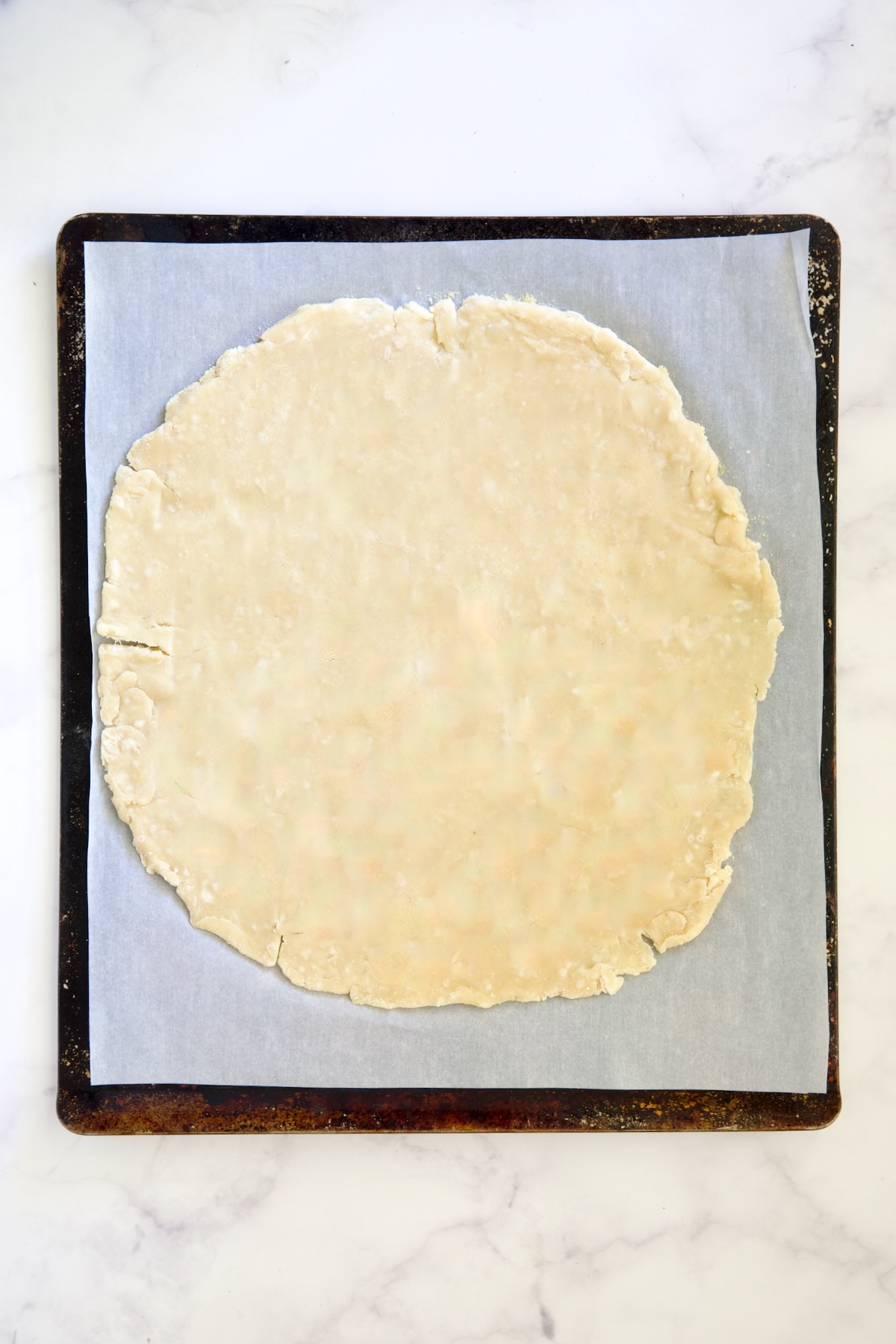 Galette dough before being filled on white parchment paper-lined baking sheet.