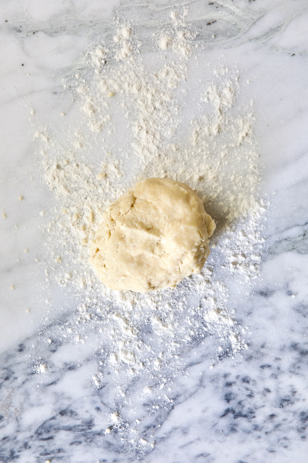 Ball of galette dough on white marble pastry board.