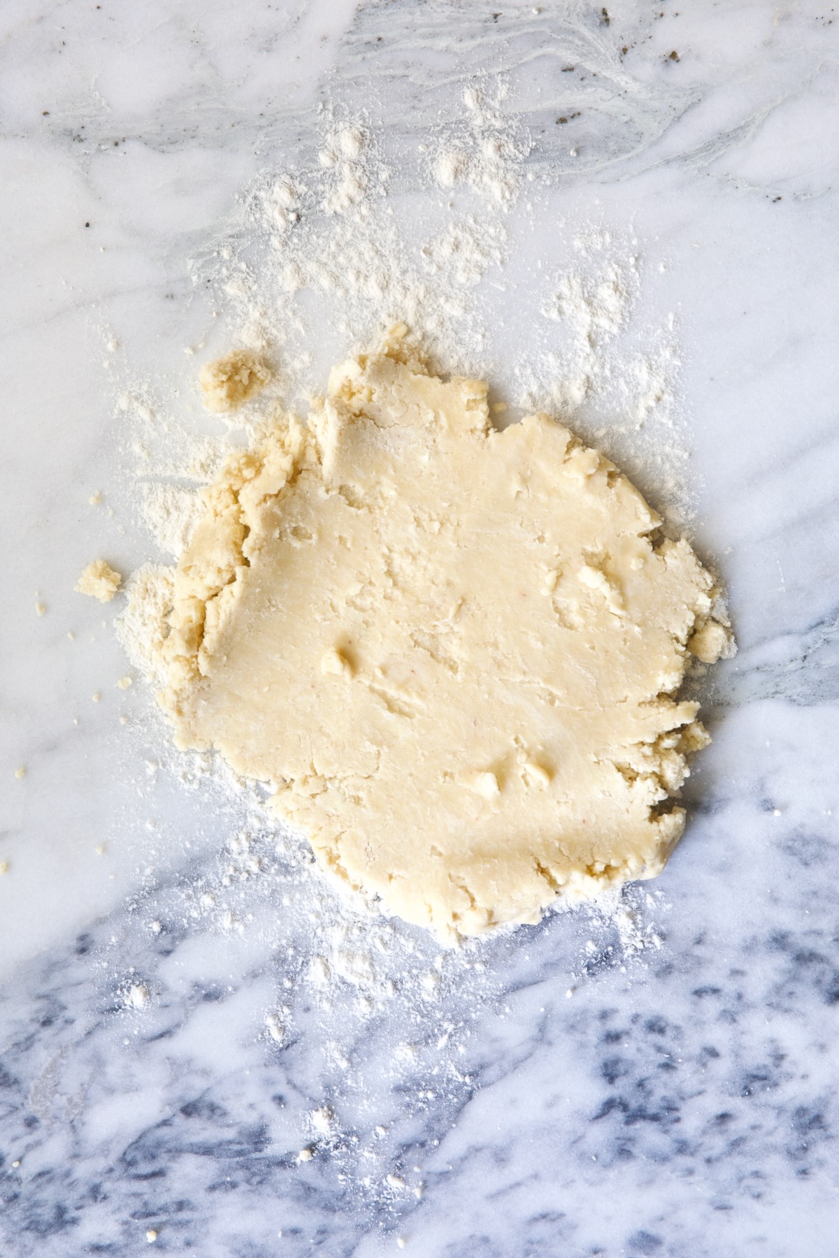 Partially rolled out galette dough on white marble pastry board.