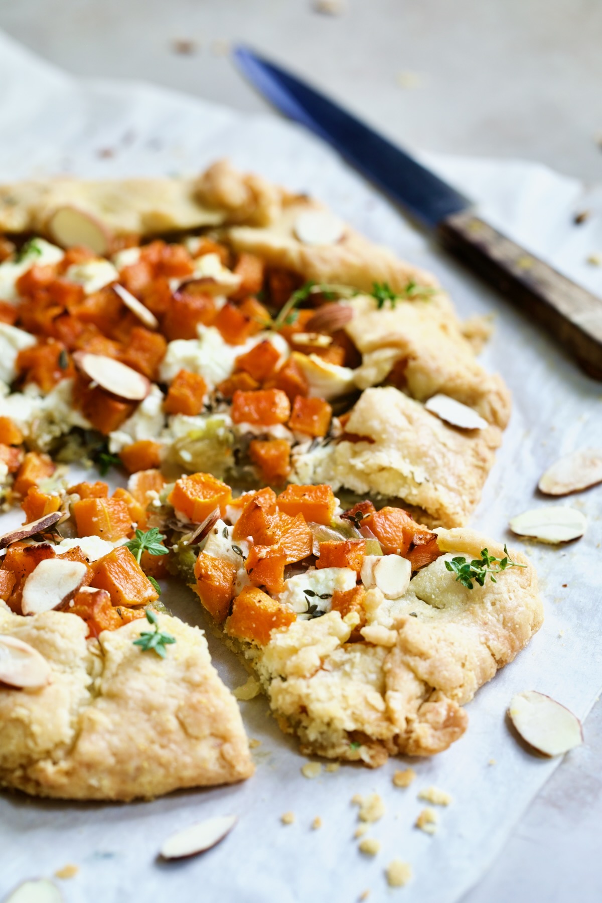 Butternut Squash Leek and Goat Cheese Galette on white parchment paper cut into wedges and garnished with sliced almonds.