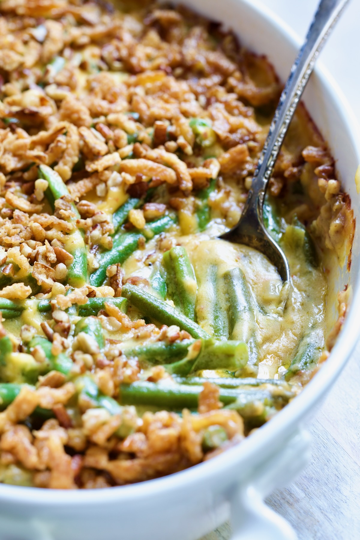 Cheesy Green Bean Casserole in white oval gratin dish with some spooned out to expose beans and sauce.