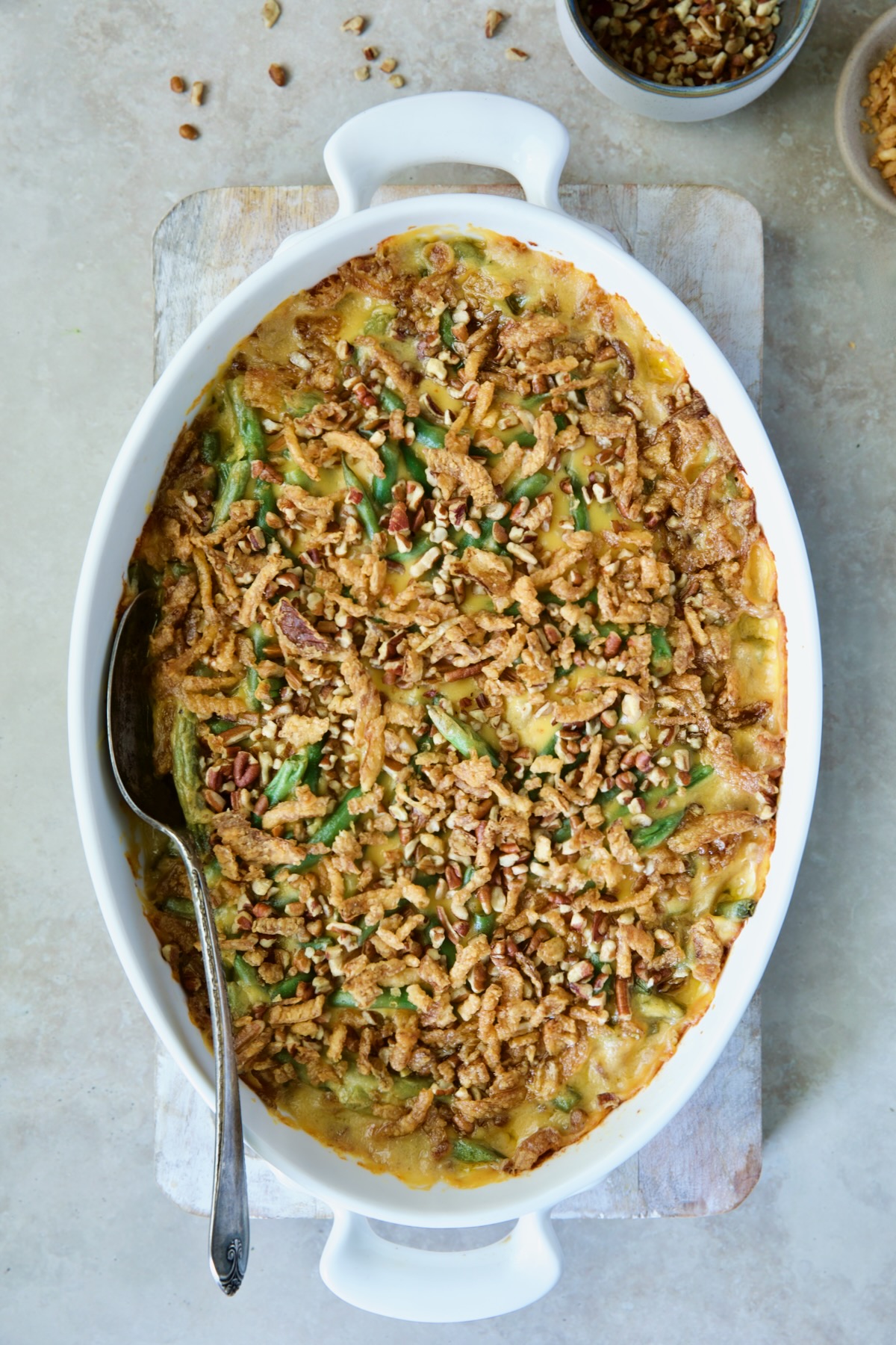 Baked Cheesy Green Bean Casserole on wood cutting board with serving spoon.