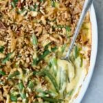 Cheesy Green Bean Casserole in white oval gratin dish with serving spoon.